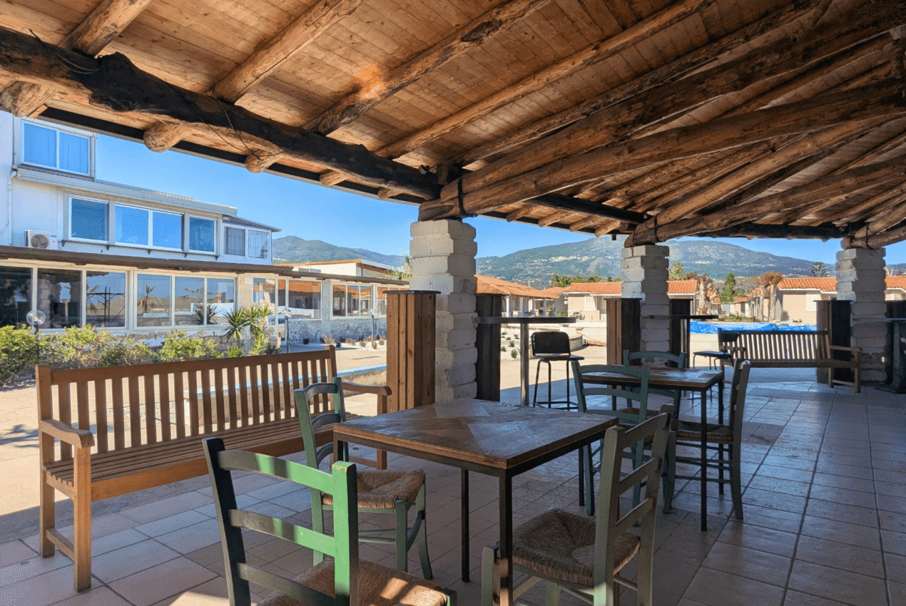 Dehors del ristorante del villaggio Patti Beach Resort con tavoli all'aperto e vista panoramica sulle colline siciliane e l'area bungalow