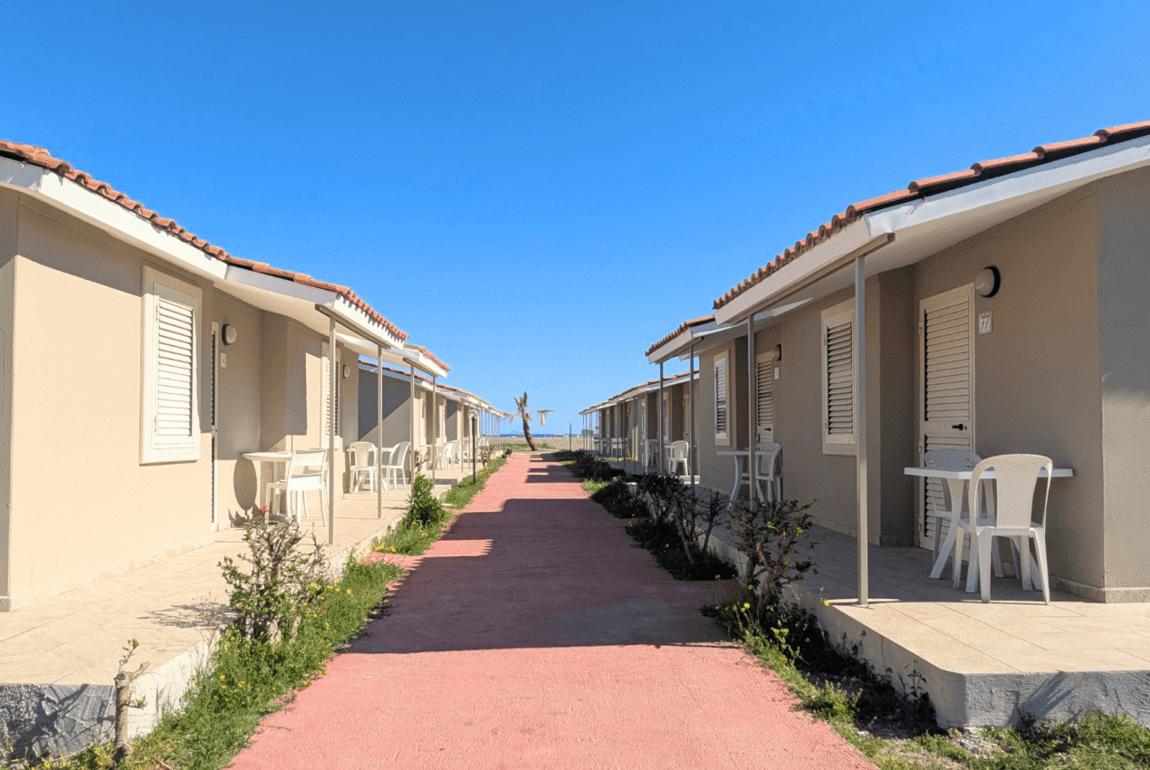 Lungo viale rosa che conduce verso il mare, fiancheggiato da bungalow con veranda privata in un villaggio vacanze a Patti con vista Eolie