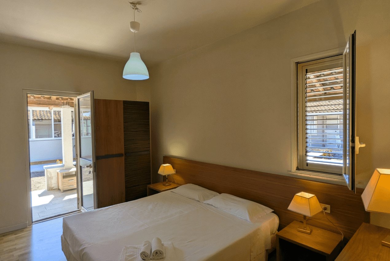 Interno di una camera matrimoniale moderna del Patti Beach Resort: arredamento in legno, illuminazione calda e accesso diretto al patio privato