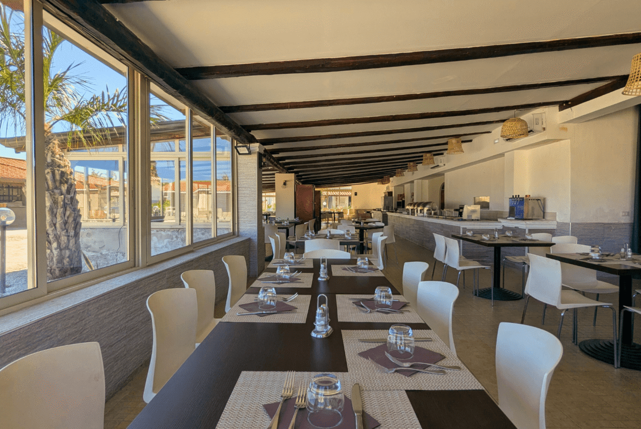 Ampia sala ristorante luminosa del Patti Beach Resort con vista sul giardino esterno e bungalow, perfetta per cene di gruppo e famiglie