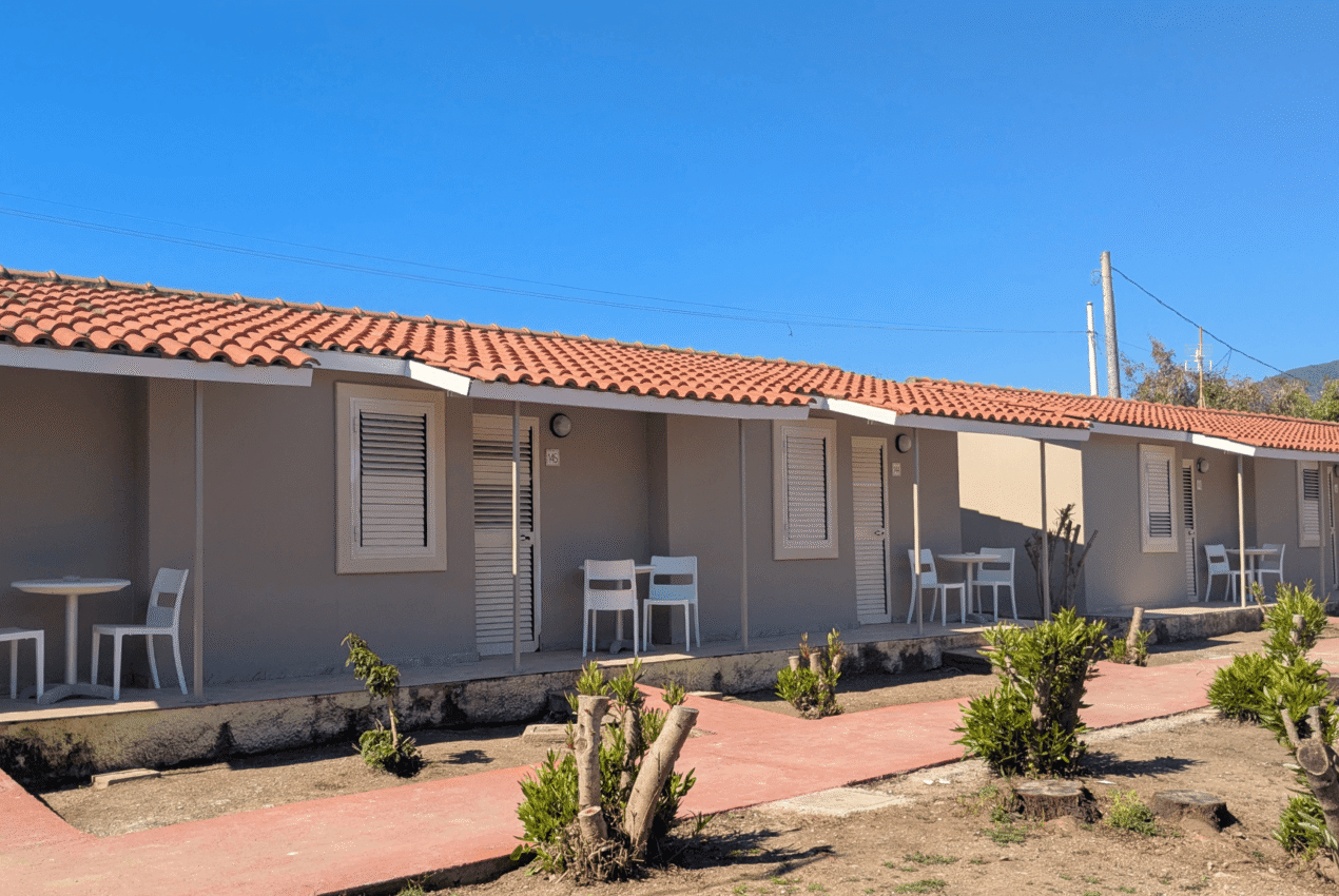 Infila di bungalow con tetto in tegole rosse e patio privato con tavolo e sedie, circondati da un giardino verde in un resort a Patti, Sicilia