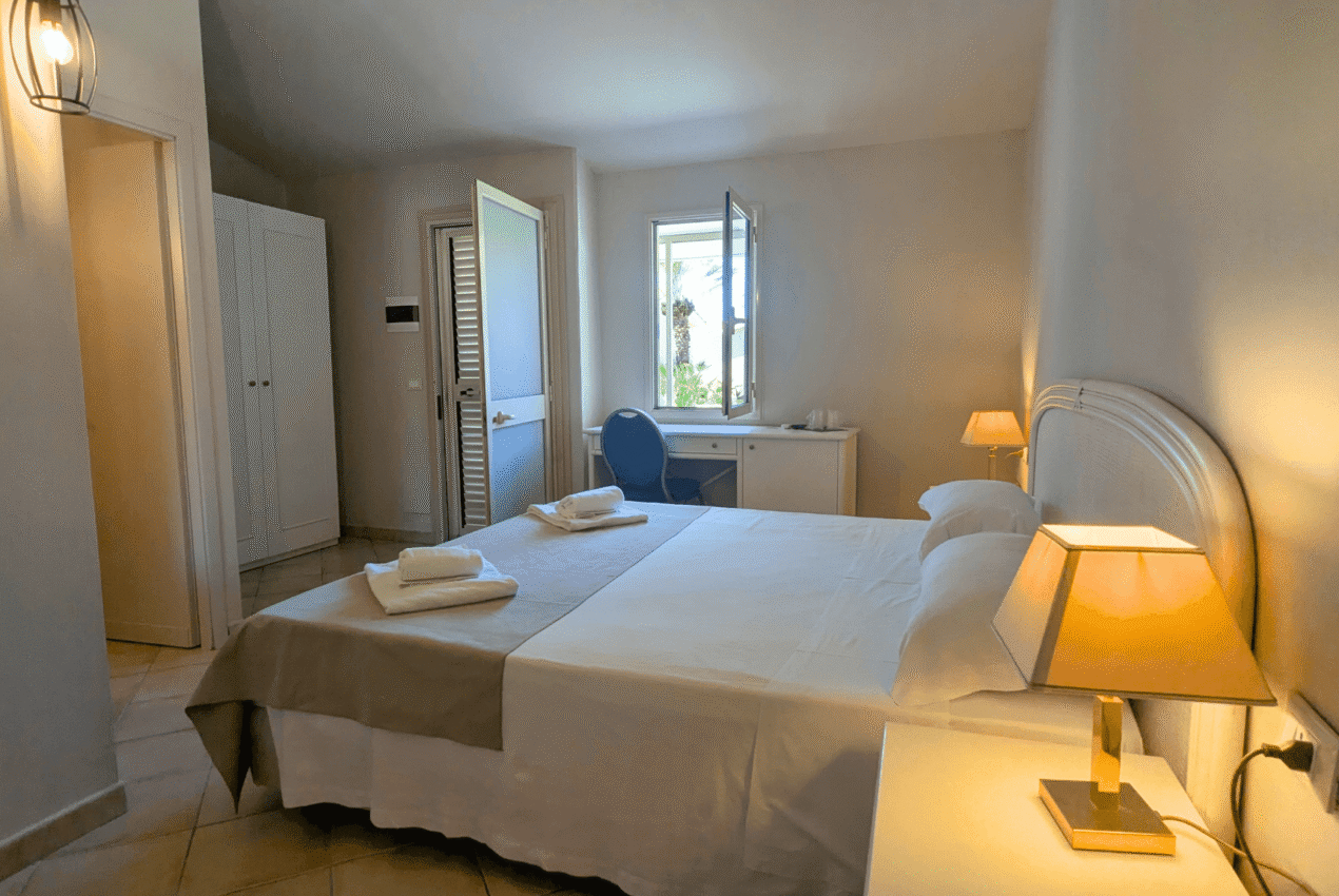 Interno di una camera doppia del Patti Beach Resort con letto matrimoniale, comodini e finestra affacciata sul giardino