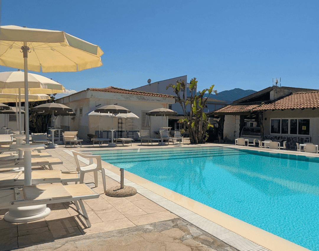 Zona solarium attrezzata con lettini e ombrelloni scuri vicino alla piscina del resort