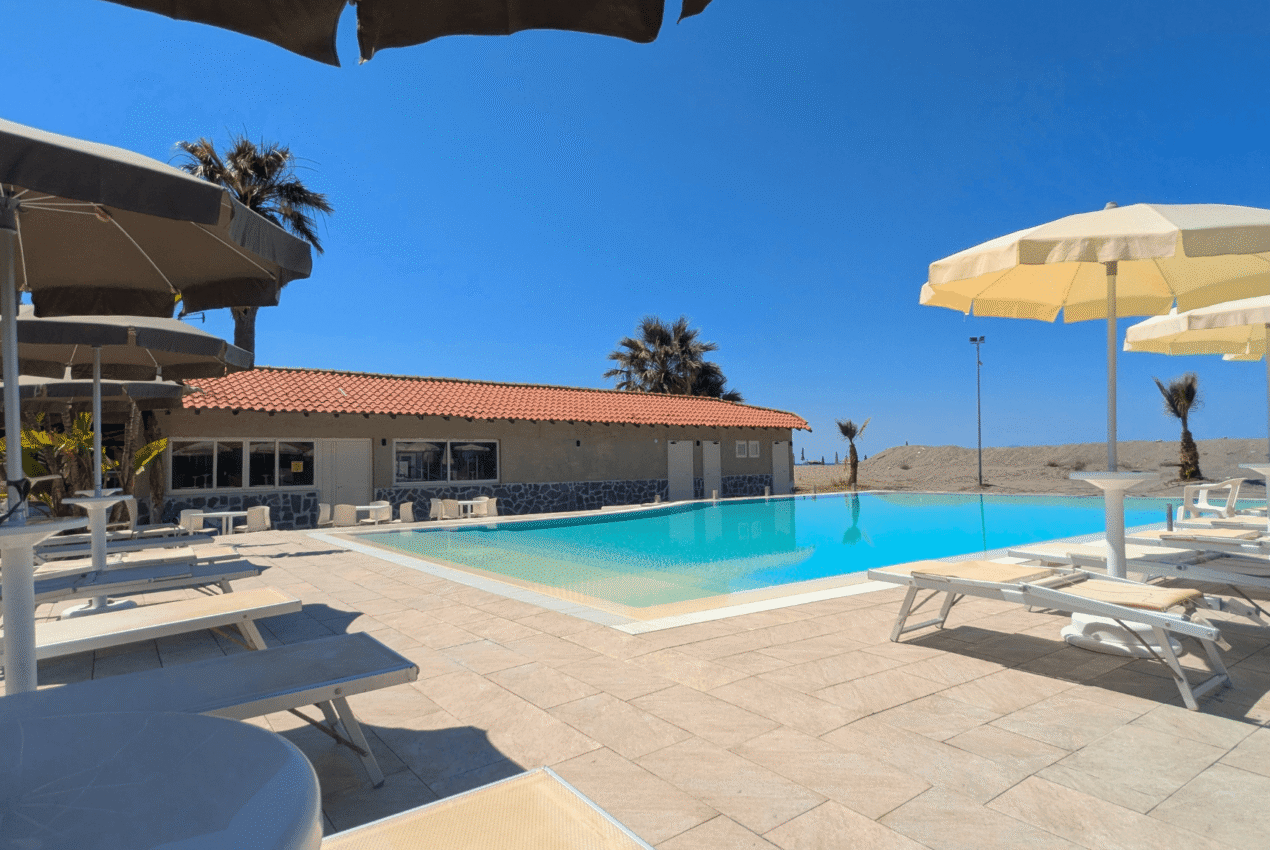 Ampia piscina all'aperto del Patti Beach Resort a Messina con palme e spiaggia sullo sfondo