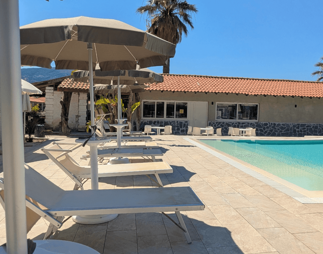 Vista ravvicinata di lettini prendisole e ombrelloni disposti lungo il bordo piscina dell'hotel