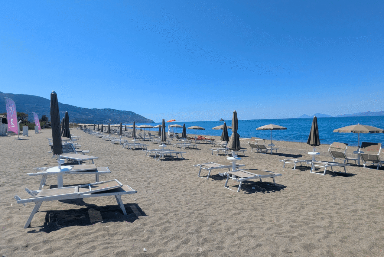 Spiaggia sabbiosa privata del resort con file di lettini e ombrelloni orientati verso il mare e le isole Eolie