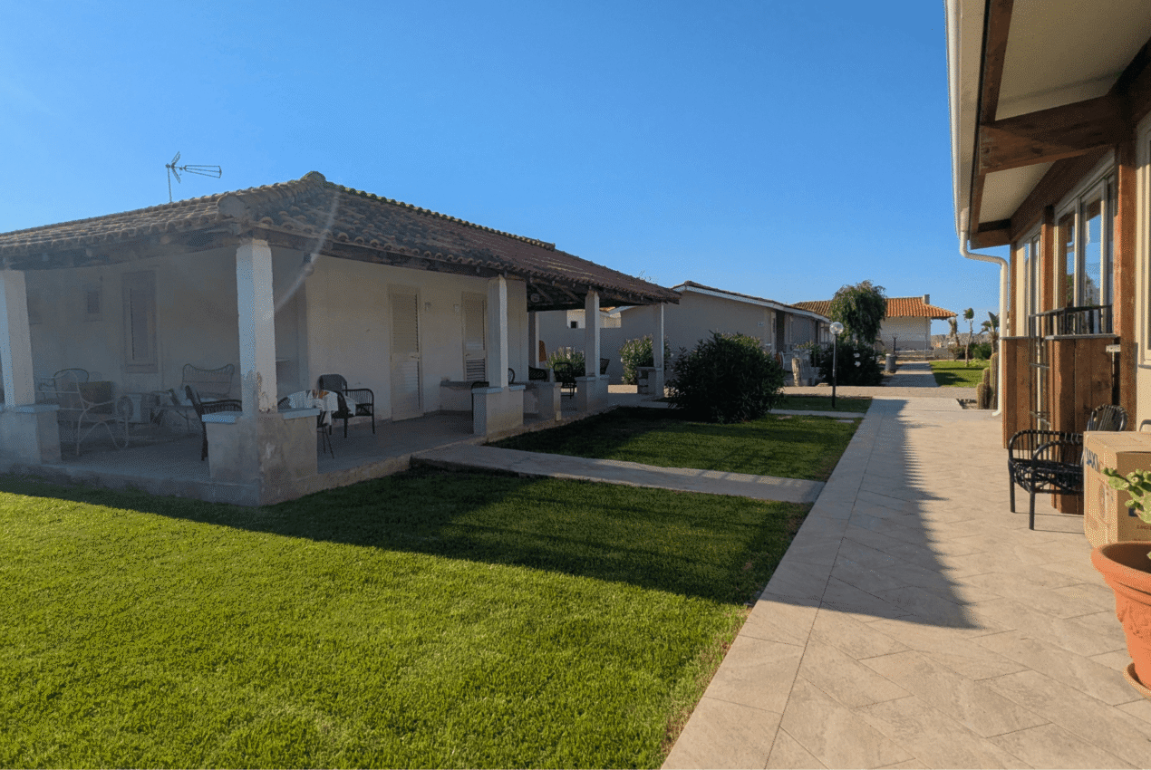 Esterno dei villini con patio privato e prato verde curato all'interno del villaggio turistico a Patti