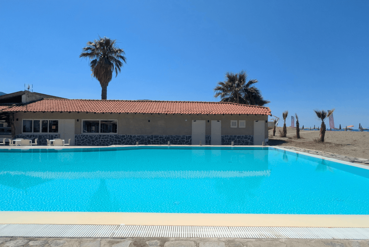 Limpida acqua della piscina del resort con riflesso degli ombrelloni e vista sulle colline di Patti